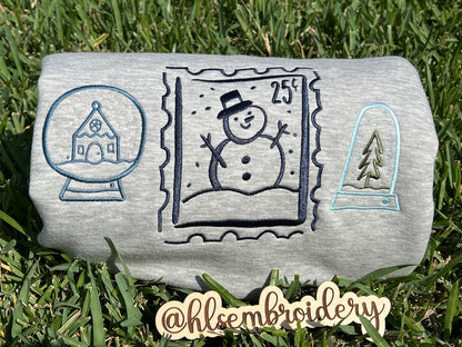 Embroidered designs of a snowman, snow globe, and pine tree on grass.