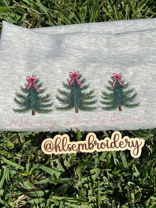 Embroidered Christmas trees with ribbons on a gray fabric background, with 'hlsembroidery' logo.