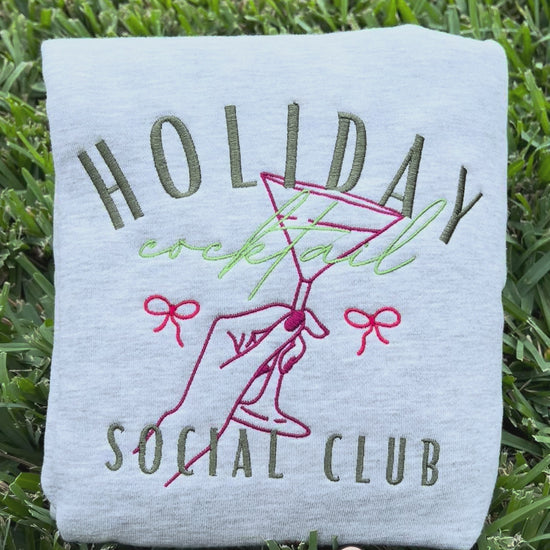 Embroidered sweatshirt with 'Holiday Cocktail Social Club' design on grass