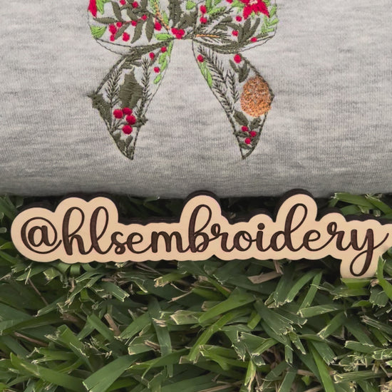 Embroidered bow design on a gray fabric with 'hlsembrodiery' branding.