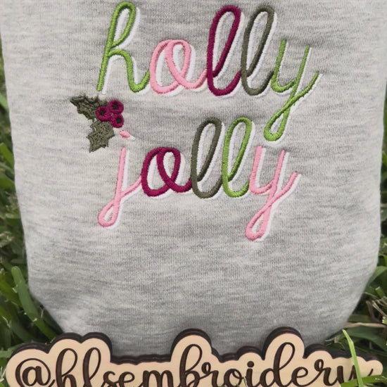 Folded gray color sweatshirt with 'holly jolly' embroidery on grass 