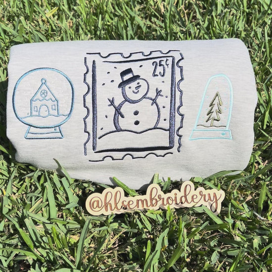 Embroidered designs of a snowman, snow globe, and pine tree on grass.