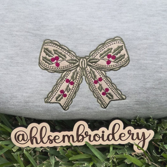 Embroidered bow design on a gray fabric with 'hlsembrodiery' branding.