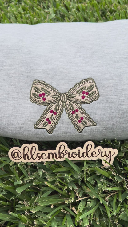 Embroidered bow design on a gray fabric with 'hlsembrodiery' branding.