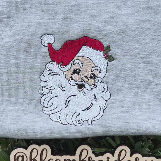 Gray sweatshirt with embroidered Santa Claus face on grass, featuring the brand hlsembroidery