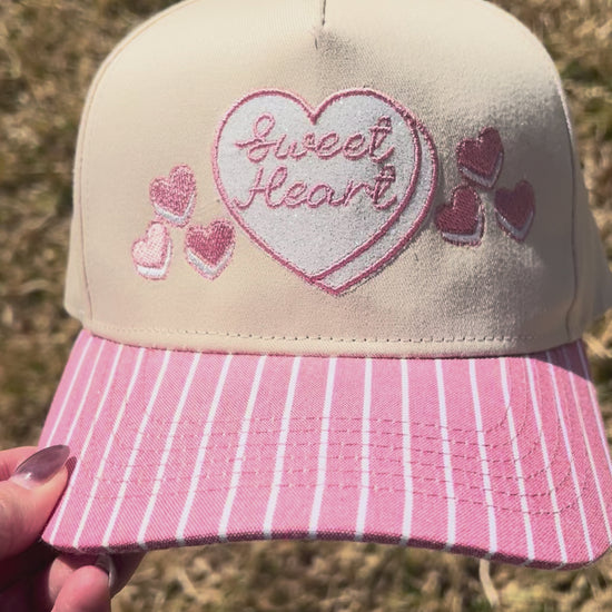 Sweet heart cap with pink and white stripped brim on grass background